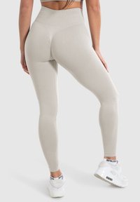 Beige hoge taille legging met textuur aan de zijkanten, strakke pasvorm en zachte stof; gecombineerd met witte sportschoenen met een logo.