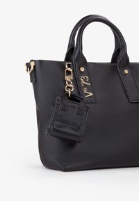 Bolso tote de cuero negro con acabado texturizado, herrajes dorados y un pequeño estuche adjunto etiquetado "SOY UNA BOLSA RESPONSABLE."