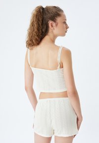 Top corto in cotone bianco con spalline rifinite in pizzo e motivo testurizzato, abbinato a pantaloni corti bianchi coordinati con un design simile e vita elastica.