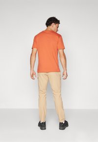 Menns uformelle antrekk med en oransje t-skjorte med korte ermer, beige cargo-bukser og svarte joggesko. Enkelt design, myk tekstur og funksjonelle lommer.