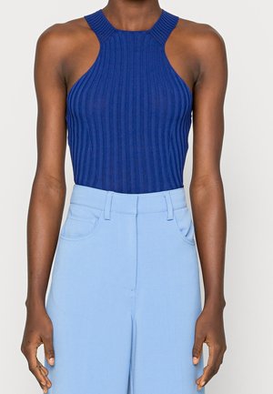 Tummansininen ribbineulottu halterneck-toppi, jossa on vartalonmyötäinen leikkaus. Yhdistetty vaaleansinisiin korkeavyötäröisiin housuihin, joissa on etutaskut ja sileä pinta.