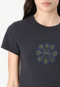 T-shirt nera a maniche corte con scollo rotondo, decorata con ricami a spirale multicolore e la parola "obey" al centro.