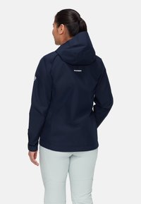 Giacca navy impermeabile con cappuccio, caratterizzata da un logo sulla schiena e polsini regolabili. Tessuto liscio, design minimalista, adatta per attività all'aperto.