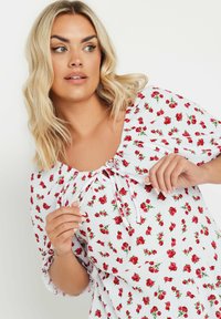 Vestido blanco con un estampado floral de pequeñas rosas rojas, con escote redondo y un detalle de lazo, y mangas cortas y sueltas. Tejido texturizado.