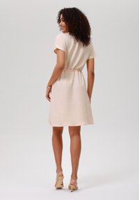 Pink textured dress with short sleeves and a drawstring waist, falling just above the knee. Worn with light-colored high-heeled shoes.