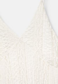 Abito bianco con tessuto testurizzato caratterizzato da strisce verticali e un design con scollatura a V. I dettagli in pizzo lungo i bordi aggiungono eleganza.