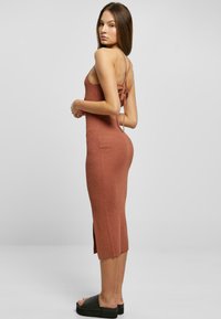 Žebrované, midi bodycon šaty v terakotové barvě s postranním rozparkem a nastavitelnými šňůrkami na zádech. Nosené s černými platformovými sandály.