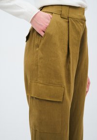 Khaki kalhoty s vysokým pasem vyrobené z lněné směsi, s bočními kapsami, plisovaným designem a volným střihem. Látka má texturovaný povrch.