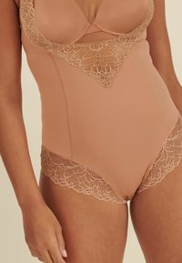 Nackter Bodysuit mit Spitzenverzierungen entlang des Ausschnitts und der Beinöffnungen, mit glattem Stoff und figurbetonter Passform.