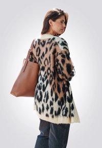 Beige en zwarte luipaardprint cardigan met een losse fit en textuurbreiwerk, gecombineerd met een bruine leren schoudertas en wijde jeans.