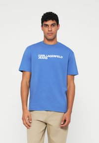 Sininen puuvillapaita lyhyillä hihoilla ja pyöreällä kaula-aukolla. Rintamuksessa valkoisella painettuna teksti "KARL LAGERFELD JEANS".