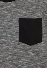 Siva prugasta tkanina s teksturiranim uzorkom, koja sadrži malu crnu patku džep na lijevoj strani. Glatka završna obrada, ležeran dizajn.