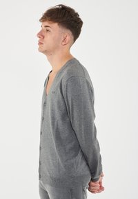 Cardigan grigio con scollo a V, maniche lunghe e chiusura a bottoni. Realizzato in un tessuto morbido, presenta un logo discreto sul petto.