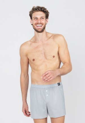 Grijze katoenen boxershorts met een knoopsluiting en elastische tailleband, voorzien van een klein logotag. De stof heeft een gladde, zachte textuur.