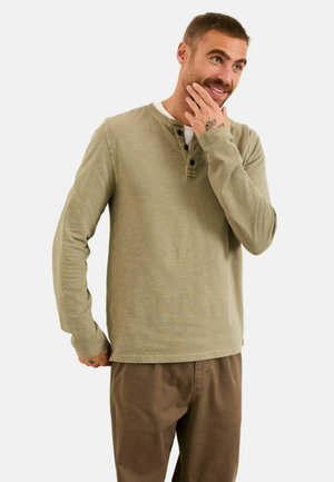 Langärmeliges Henley-Shirt in Olivgrün mit einer dreiknöpfigen Knopfleiste und gerippter Struktur, kombiniert mit braunen Chinos.