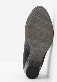 Semelle de chaussure en cuir noir présentant une surface en caoutchouc texturé avec un motif ondulé et un logo. Design à bout rond et talon bas et large.