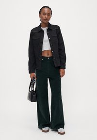 Zwarte denimjas met studaccenten, grijze cropped top, groene corduroy broek met wijde pijpen en een zwarte handtas met zilverkleurige hardware.