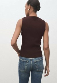 Donker bordeauxkleurig mouwloos topje met een geribbelde textuur. Gecombineerd met strakke blauwe denim jeans met achterzakken en een tailleband.