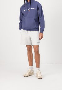Marinblå hoodie med vit text "NEW BALANCE", grå svettshorts och beige sneakers med texturerade detaljer. Enkel, avslappnad atletisk klädsel.