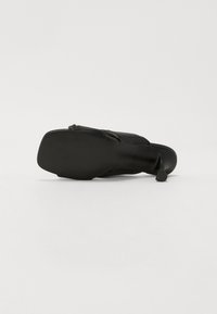 Scarpa nera con tacco alto, caratterizzata da una parte superiore in pelle liscia e una suola in gomma texturizzata; presenta un tacco sottile e un design aperto sul retro.