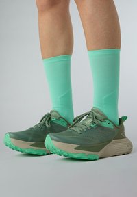 Scarpe da ginnastica verdi con tomaia in rete testurizzata, dettagli beige e suola robusta. Abbinate a calze di lunghezza ginocchio di un vivace verde menta.