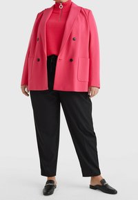 Jasnoróżowa marynarka dwurzędowa z czarnymi guzikami, w połączeniu z czerwoną golfem i luźnymi czarnymi spodniami. Czarne buty wsuwane z detalem w postaci łańcucha.