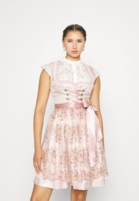 Robe dirndl rose clair avec corsage en dentelle, manches courtes et ceinture en satin. Des détails floraux et des bordures en dentelle rehaussent l'apparence de la jupe.