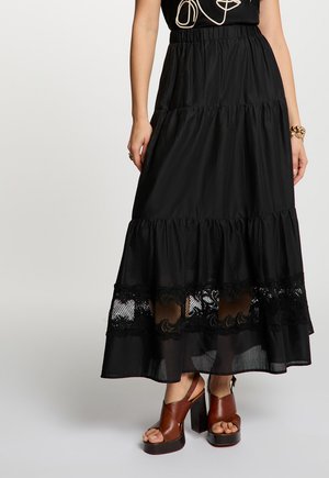 Donna che indossa una gonna nera a balze con inserti in pizzo sopra l'orlo e sandali con plateau e tacchi alti marroni.