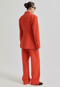 Oransje skreddersydd dress med en strukturert blazer og vide bukser, laget av glatt stoff med en ren finish og minimalt med detaljer.