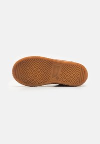 Suela de zapato de goma en marrón con un patrón geométrico texturizado. Presenta un detalle de marca y un borde liso y redondeado a lo largo del perímetro.