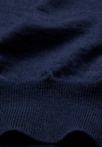 Marineblaues Strickgewebe mit glatter Textur und geripptem Rand. Leicht gedehnt, um die Detailgenauigkeit im Gewebe und die Texturvariationen zu zeigen.