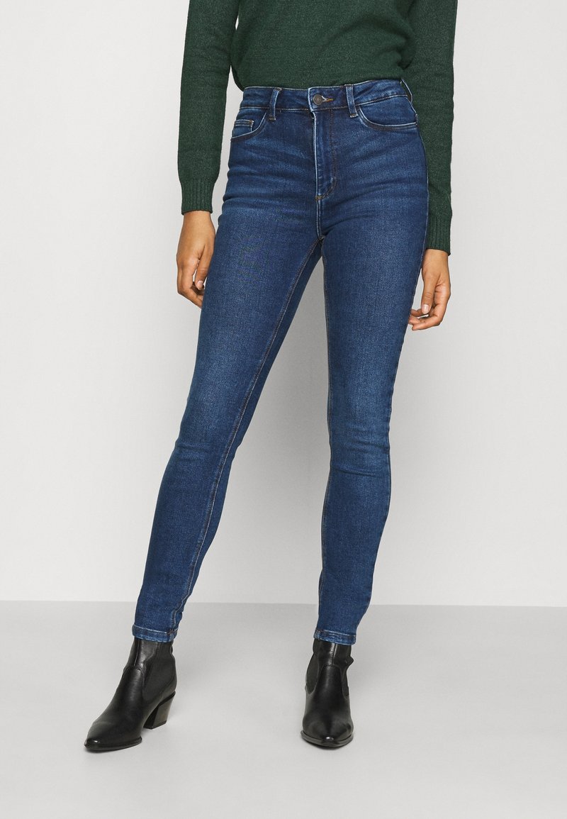 Smala jeans i mörkblå denim med en slät yta, hög midja och kontrasterande sömmar. Matchas med svarta ankelskor.