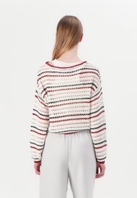 Crochet sweater with a loose fit, featuring alternating stripes in cream, red, and navy. Short sleeves and a wide neckline.