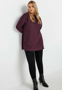 Lång, ribbad, mörk burgundy tröja med avslappnad passform, kombinerad med svarta skinny jeans och spetsiga svarta ankboots.