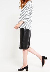 Gestreept wit en zwart langharig topje, zwarte leren midi-rok en zwarte laarzen met hak van lakleer. Schone lijnen, casual silhouet, zijslits.