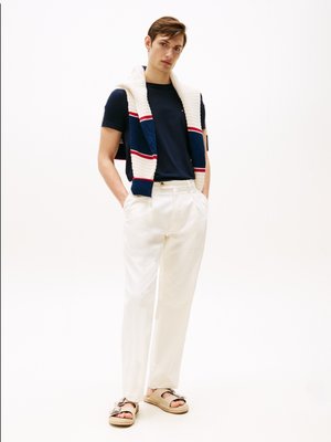 T-shirt navy abbinato a pantaloni crema, con un maglione testurizzato bianco e blu appoggiato sulle spalle e sandali marroni con fiocchi.