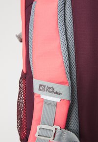 Backpack strap in pink and purple fabric, featuring grey mesh padding and a grey buckle with logo detail. Textured surface visible.
