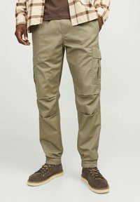 Khaki cargobroeken hebben zijzakken, elastische boorden en een gladde, duurzame stof. Gekoord met bruine veterschoenen en een geruit shirt.