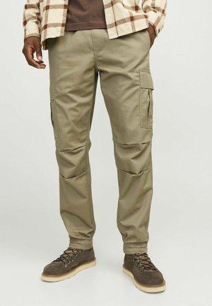 Pantalonii cargo khaki au buzunare laterale, manșete elastice și un material neted, durabil. Sunt purtați cu bocanci maronii cu șireturi și o cămașă în carouri.