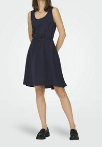 Robe sans manches bleu marine avec un col rond, taille élastique et jupe évasée. Associée à des mocassins noirs sur un fond clair.