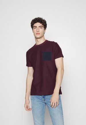 Camiseta de algodón a rayas burdeos con un bolsillo azul marino. Mangas cortas y cuello redondo. Textura suave y corte casual.