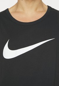 Svart linne med en framträdande vit Nike swoosh-logotyp i mitten, tillverkat av mjukt tyg med rund halsöppning.