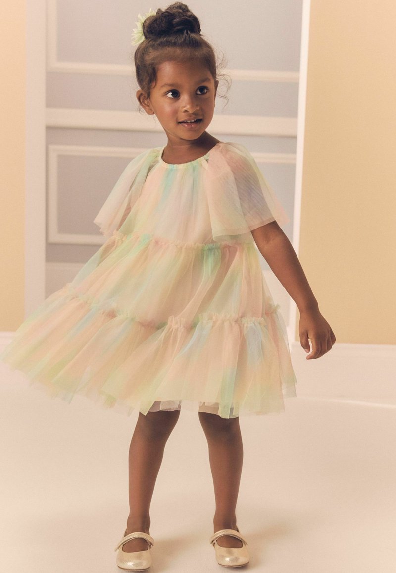 Robe en tulle pastel ornée de volants superposés avec une texture douce et translucide. Associée à de simples chaussures métalliques, elle offre un design ludique.