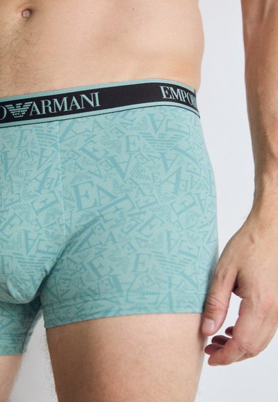 Boxeri scurți de culoare albastru deschis, cu un model logo pe tot materialul în nuanțe variate. Chingă elastică neagră cu textul "EMPORIO ARMANI".