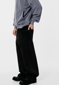 Hanorac oversized gri, cu buzunar frontal, asortat cu pantaloni lejeri din catifea cord cu negru. Pantofi masivi negri completează ținuta.