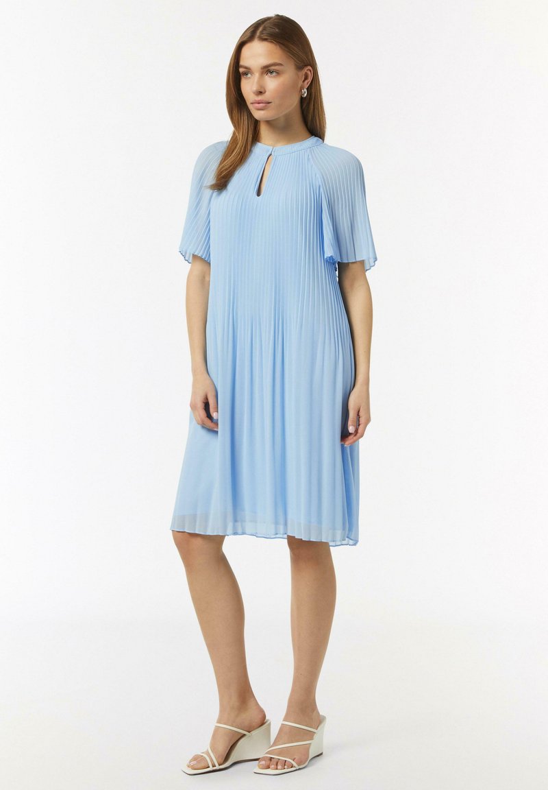 Himmelblaues Faltenkleid mit kurzen Ärmeln und einem Schlüsselloch-Ausschnitt. Der Stoff wirkt fließend und weich. Tragen mit weißen Keilsandaletten.