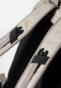 Lichtbeige rugzakbanden met zwarte sluitingen en webbing, met een gladde oppervlakte en nette stiksels langs de randen.