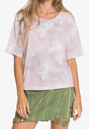 Różowa koszulka typu tie-dye z krótkimi rękawami i luźnym krojem, w połączeniu z zieloną spódnicą z białymi paskami i ozdobnymi elementami.