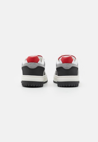 Sneakers con una toma in suede grigio, dettagli in pelle nera, linguetta rossa sul tallone e suola intermedia bianca. La suola presenta un motivo in gomma nera testurizzata.