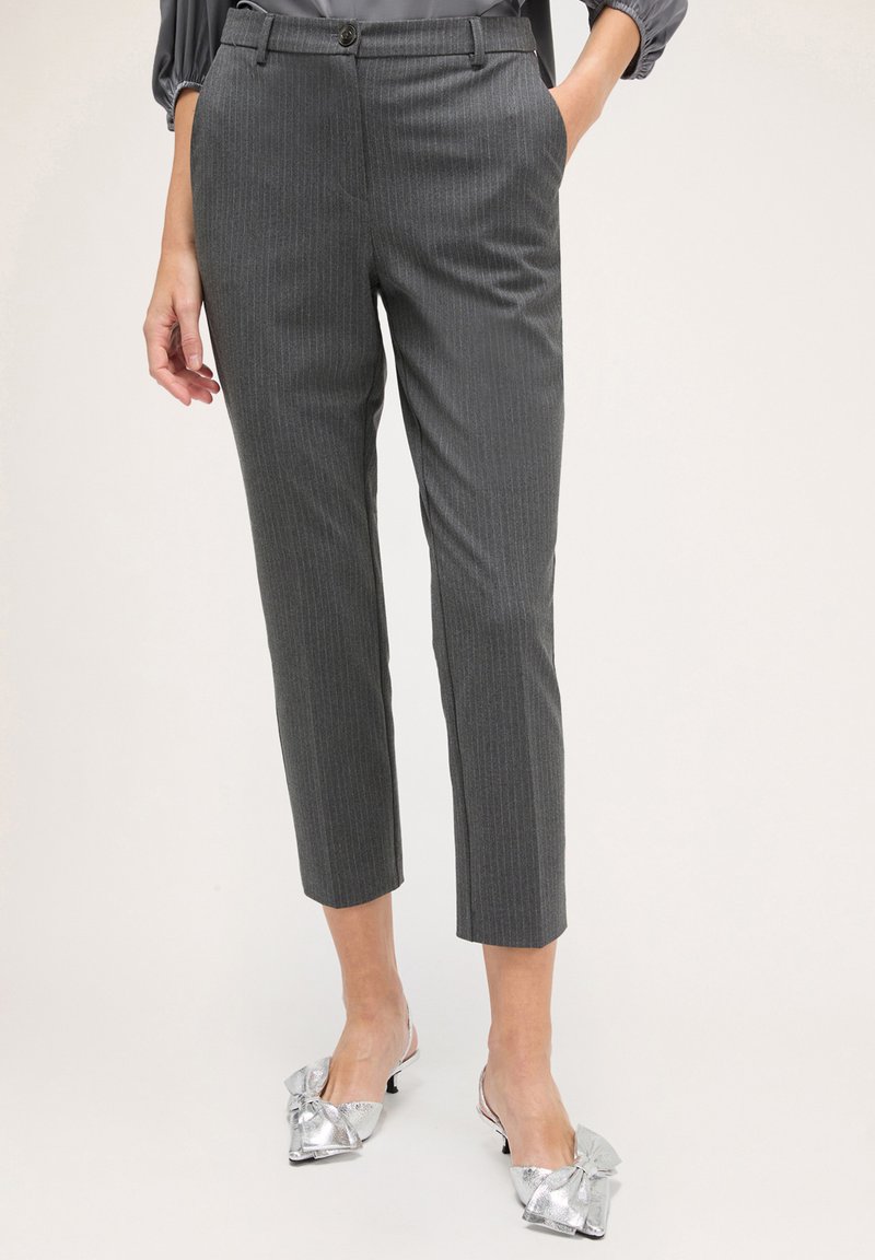 Pantaloni grigi a righe sottili con vestibilità sartoriale, lunghezza cropped e una texture del tessuto liscia. Abbinati a calzature argentate con un dettaglio a fiocco.